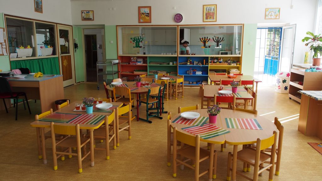 Jídelní část třídy s prostřenými stolky a výdejním okénkem do kuchyně